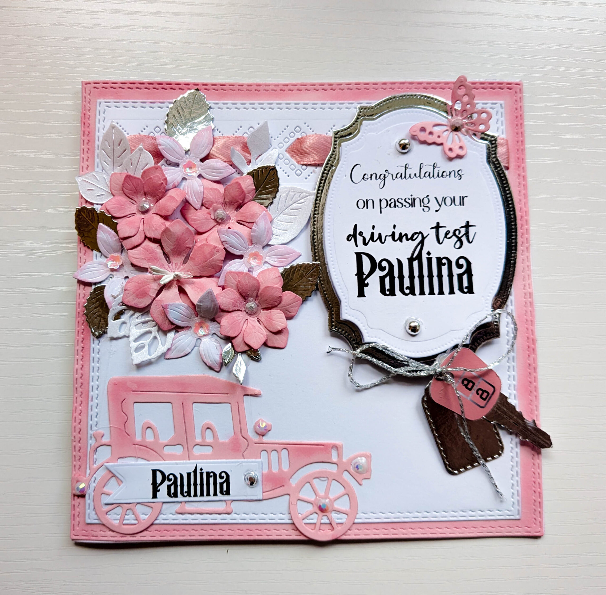 Front view of handmade pink 15cm driving test card featuring vintage car cut-out, 3D paper flowers, and silver mirror details.