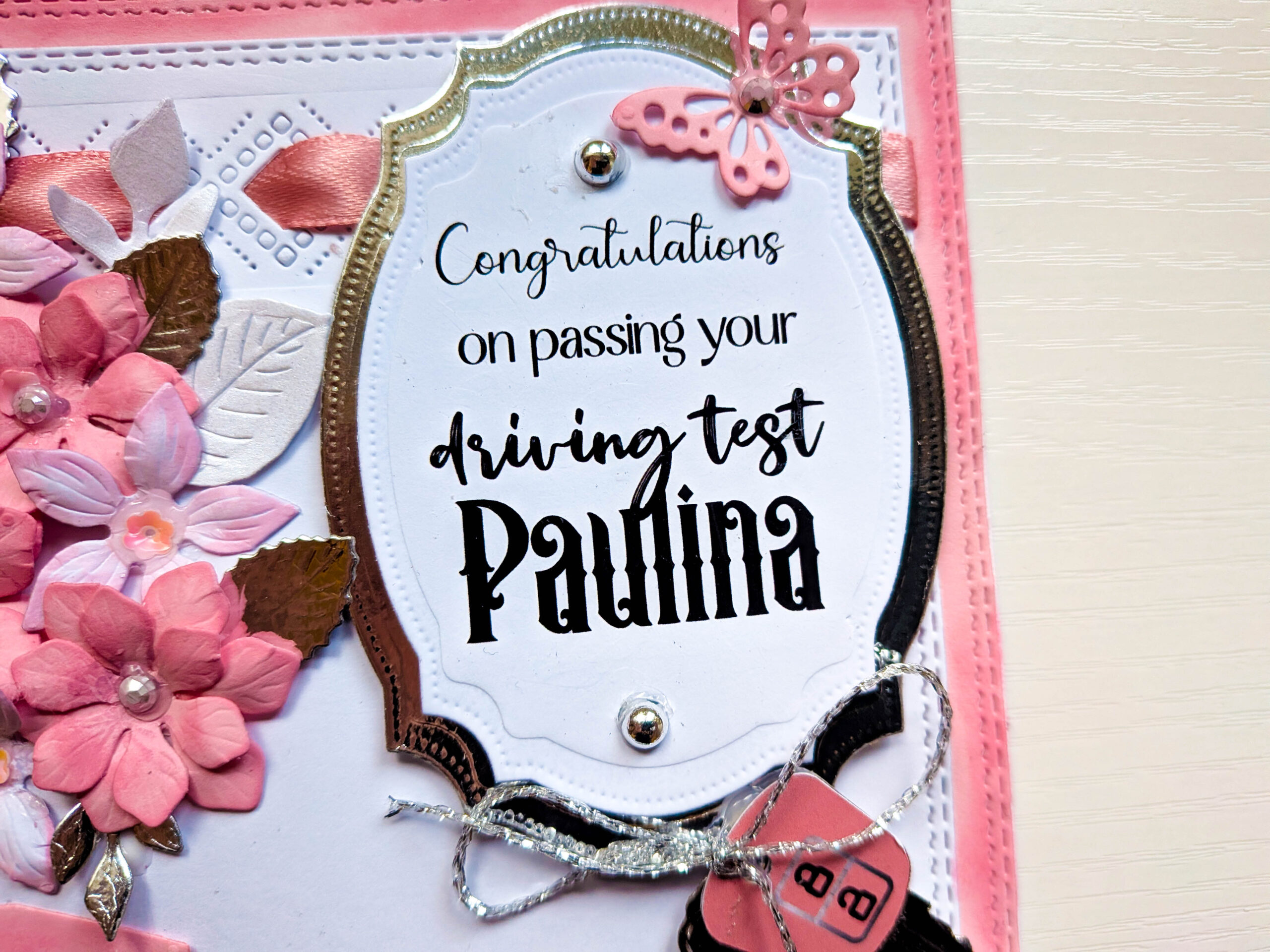 Close-up of personalised ornate oval plaque reading Congratulations on passing your driving test Paulina with silver butterfly and pearl gems.
