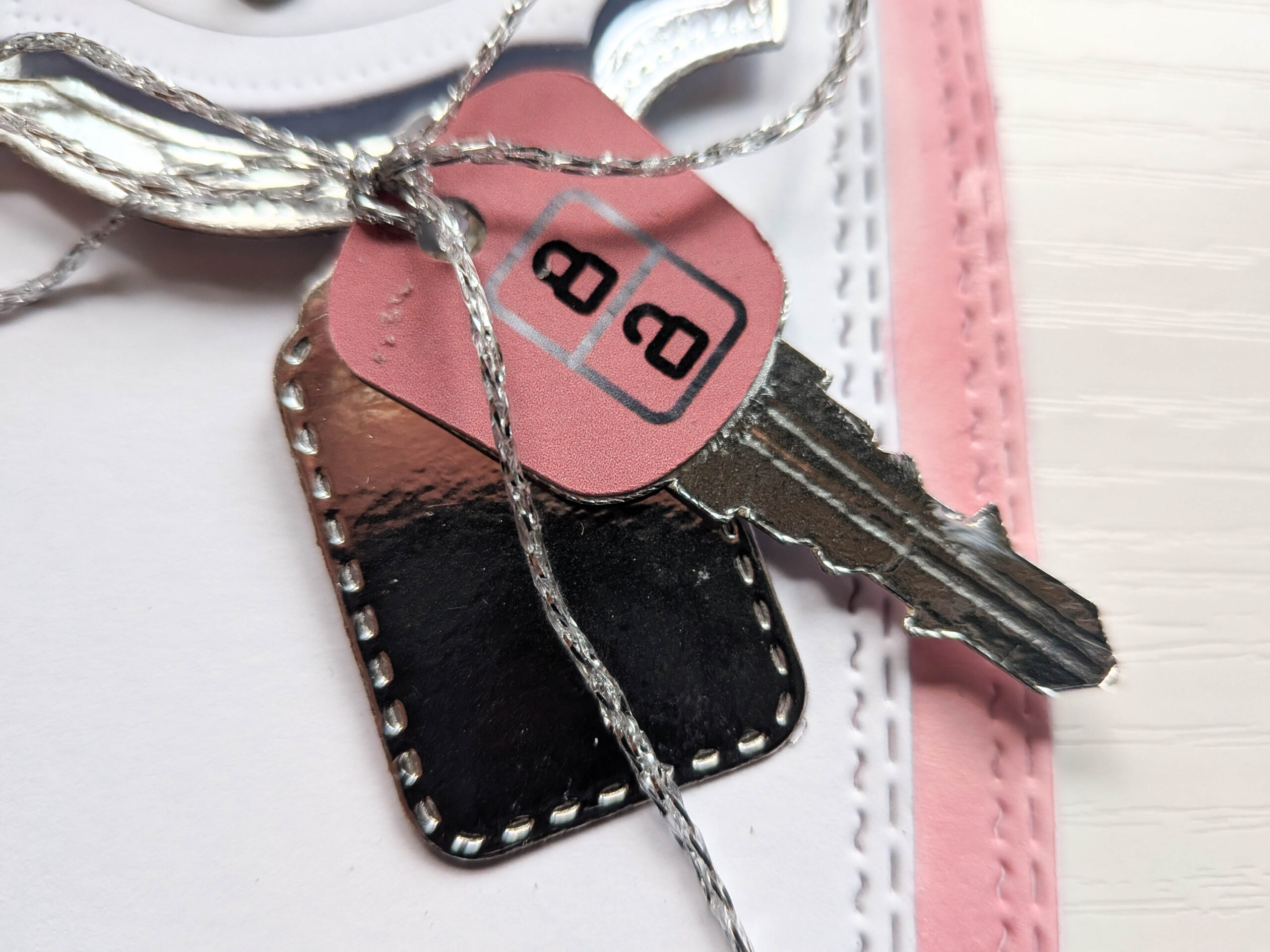 Close-up of handmade 3D die-cut paper car keys and key fob charm tied with fine silver thread.