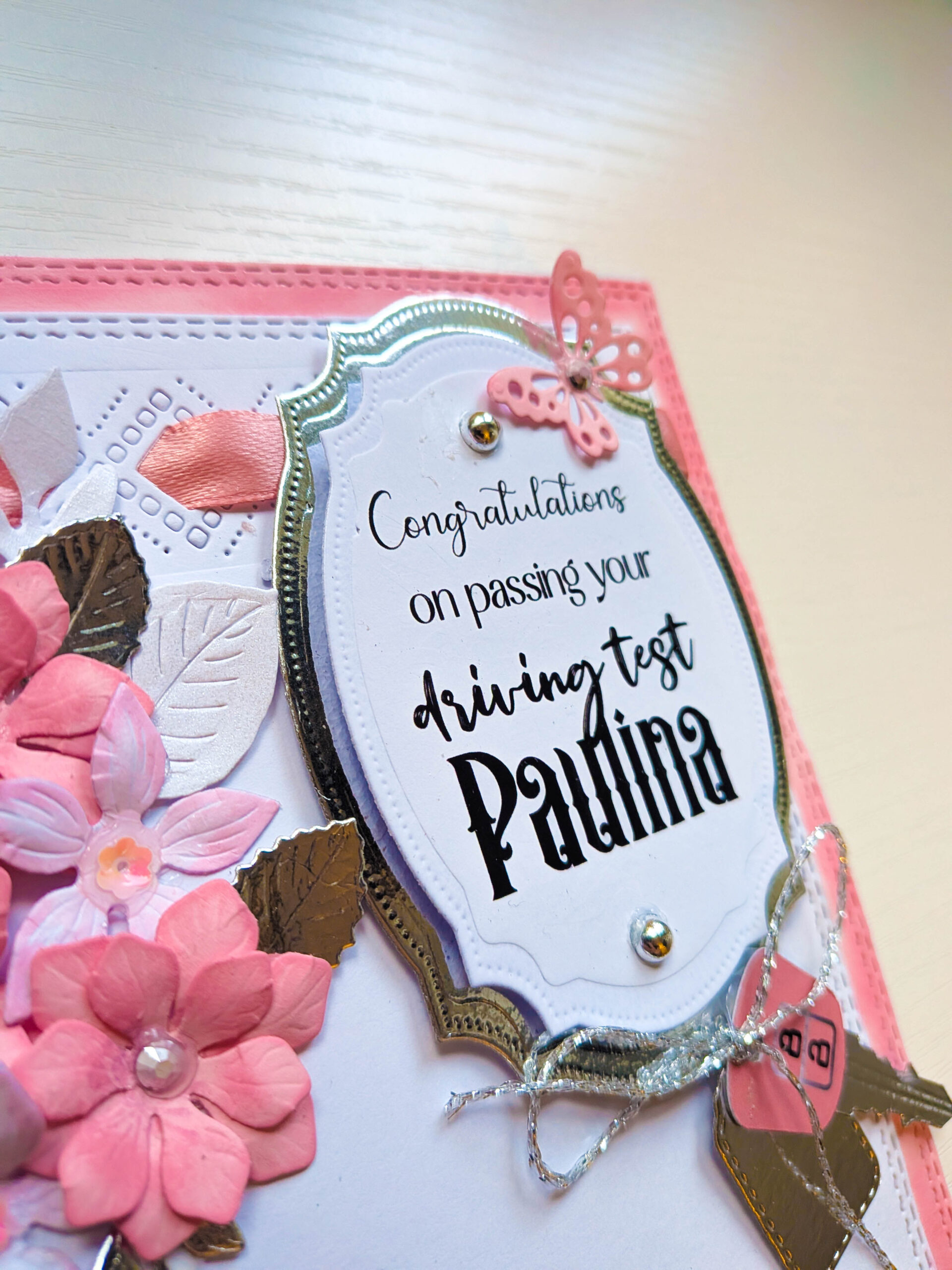 Close-up of personalised ornate oval plaque reading Congratulations on passing your driving test Paulina with silver butterfly and pearl gems