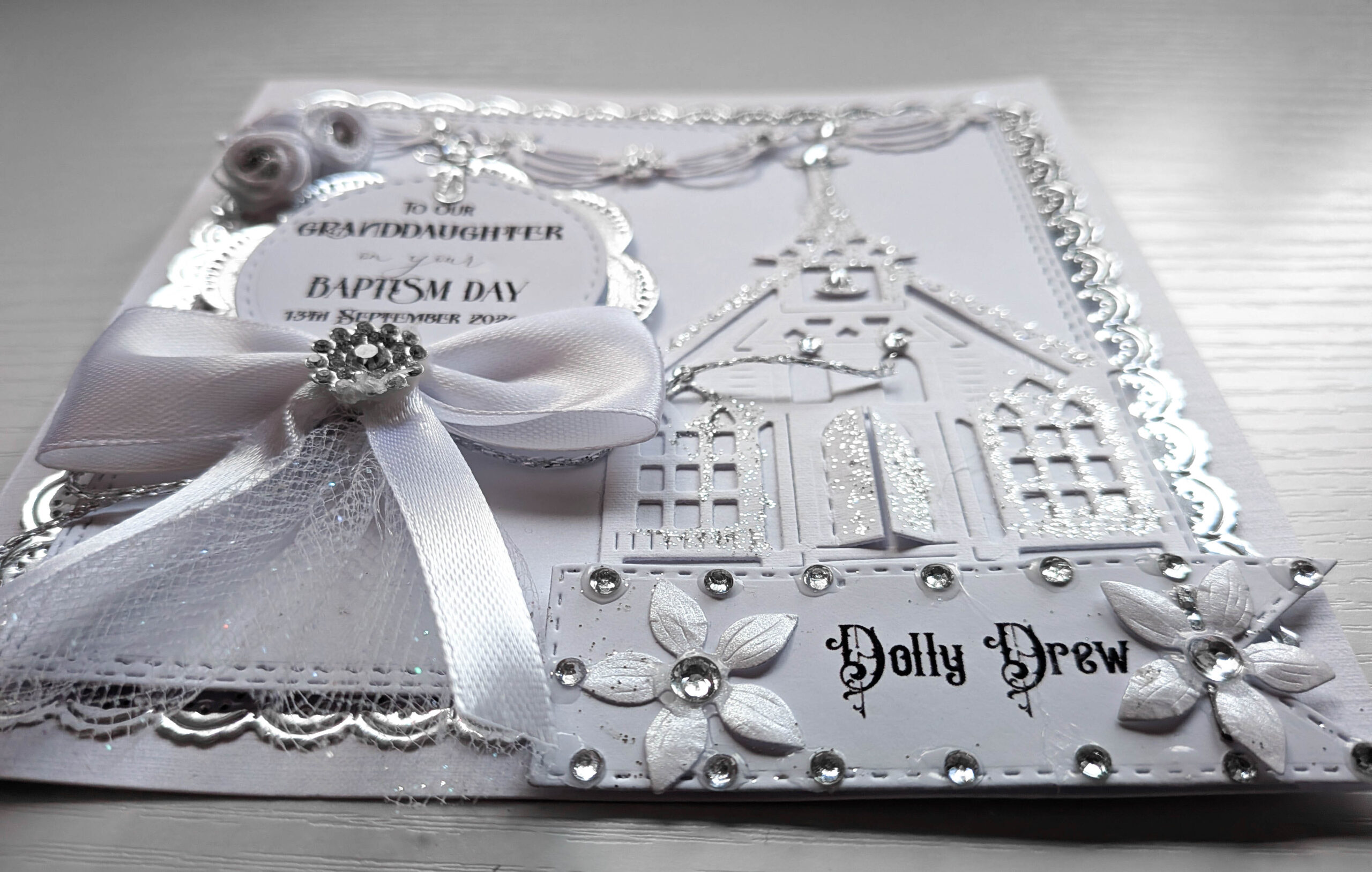 Close-up of crystal brooch on satin bow and embossed church cardstock with silver glitter details.